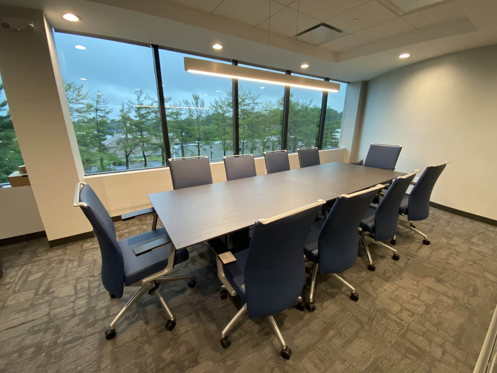 Long boardroom table with navy executive chairs, windows running the length of one wall