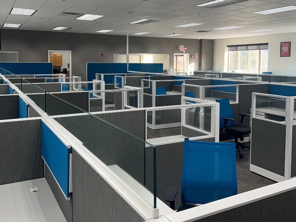 Rows of cubicles with blue screens, seen down the aisle
